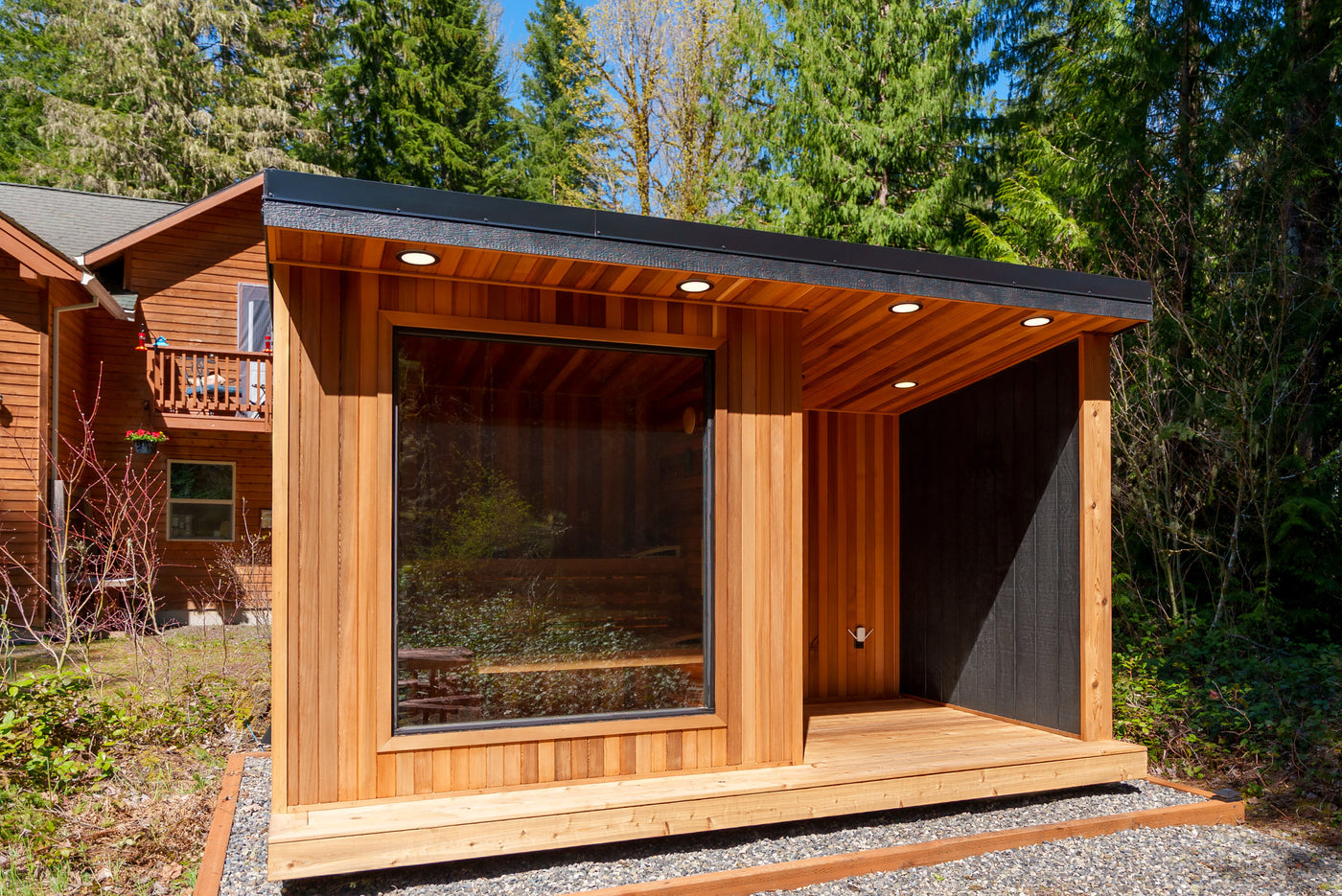 Hand-built cedar sauna by NW Immersion set on a gravel pad beside a forested home